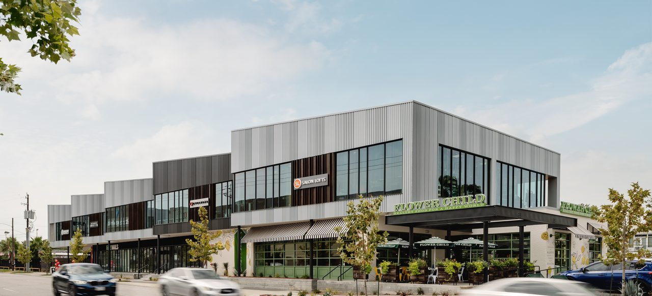 The Flower Child corner at Market at Houston Heights, with Salon Lofts on the second floor and cars passing along North Shepherd Drive